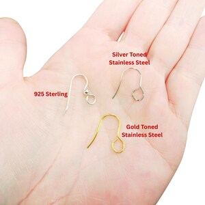 May include: Three metal earring hooks in different finishes. One is labeled 925 Sterling, one is labeled Silver Toned Stainless Steel, and one is labeled Gold Toned Stainless Steel. Each hook features a curved wire design with a small loop at the end.