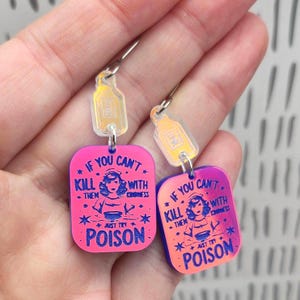 May include: A pair of dangle earrings featuring rectangular acrylic charms with a pink and orange gradient. The charms display a graphic of a person and the text: IF YOU CAN'T KILL THEM WITH KINDNESS JUST TRY POISON. Small bottle-shaped charms are attached.