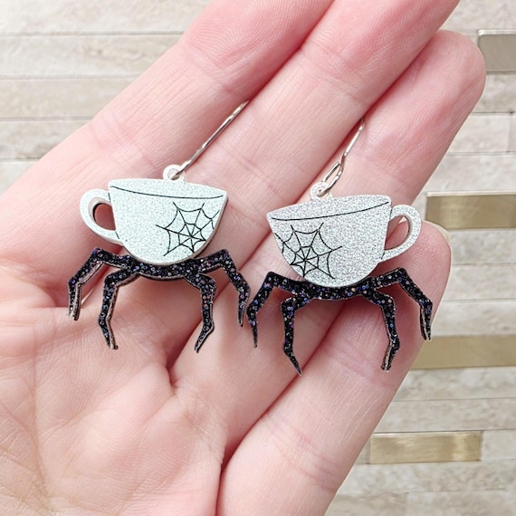A tiny spider living inside a teacup, rendered in acrylic as earrings — delightfully unhinged Halloween statement jewelry with 62 favorites proving real demand.