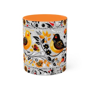 May include: A ceramic mug with an orange rim and a gray background. The mug features a repeating pattern of stylized black and yellow birds perched on branches with orange and red flowers.