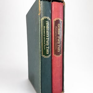 May include: A two-volume set of hardcover books housed in a slipcase. The green volume is titled Andersen's Fairy Tales illustrated by Arthur Szyk, and the red volume is titled Grimms' Fairy Tales illustrated by Fritz Kredel, both with gold text.