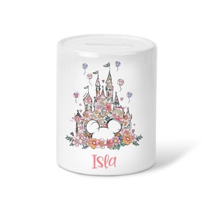 May include: White ceramic money box featuring a floral castle design with Mickey Mouse ears. The castle is decorated with pink, yellow, and peach flowers. The name "Isla" is written in pink script below.
