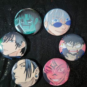 May include: A collection of six round buttons featuring anime character illustrations. The buttons showcase various characters with distinct facial expressions and color schemes, including shades of blue, green, pink, and black. The buttons are arranged on a dark, textured surface.