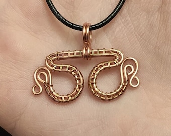 May include: A copper wire necklace with a pendant shaped like the number 55. The pendant is made of wire that is wrapped around itself to create a three-dimensional design. The necklace is on a black cord.