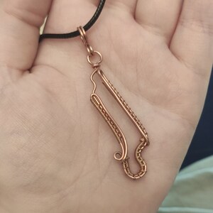 May include: A copper wire necklace with a pendant shaped like a stylized letter S. The pendant is made of multiple strands of wire that are twisted and woven together.