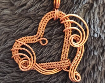 May include: A copper wire heart pendant necklace with a woven design and intricate swirls. The pendant is a unique and handmade piece of jewelry.