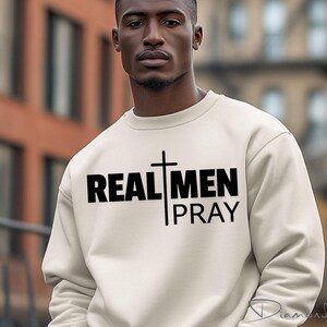 May include: A white sweatshirt with black text that reads "REAL MEN PRAY" and a black cross graphic.