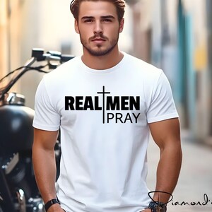 May include: White t-shirt with a black cross and the text "REAL MEN PRAY" printed on the front.