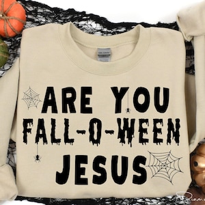 May include: A beige sweatshirt with the text "Are you Fall-O-Ween Jesus" printed in black. The text is dripping and has spiderwebs and spiders around it.