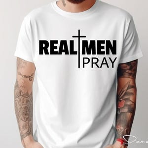 May include: White t-shirt with black text that reads "REAL MEN PRAY" and a black cross graphic.