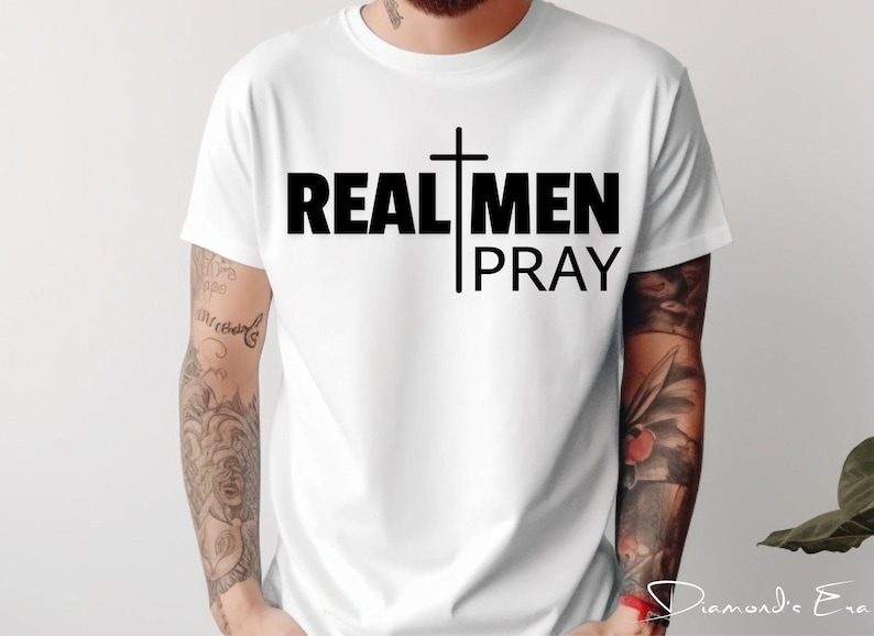 May include: White t-shirt with black text that reads "REAL MEN PRAY" and a black cross graphic.