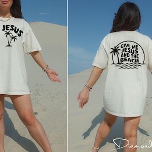 以下が含まれることがあります： 白地に黒いパームツリーと「Jesus」の文字がプリントされたTシャツ。後ろには「Give me Jesus and the beach」の文字がプリントされている。