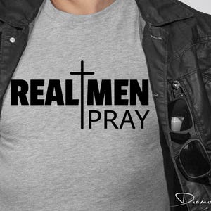 May include: A gray t-shirt with the text "REAL MEN PRAY" and a cross graphic.