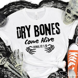 May include: White t-shirt with black text that reads "Dry Bones Come Alive Ezekiel 37:1-10" and two black skeletal hands on either side of the text.