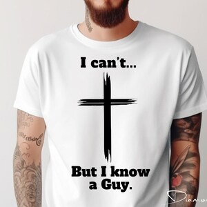 May include: White t-shirt with black text that reads "I can't... But I know a Guy." and a black cross graphic.