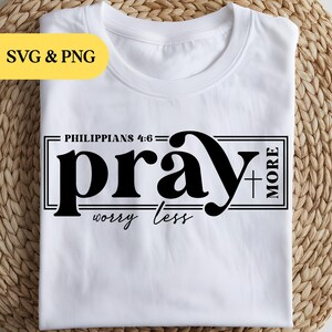 May include: A white short-sleeved t-shirt featuring black text that reads Philippians 4:6, pray more, and worry less, with a small cross symbol integrated into the design. The graphic is enclosed within a rectangular black line border.