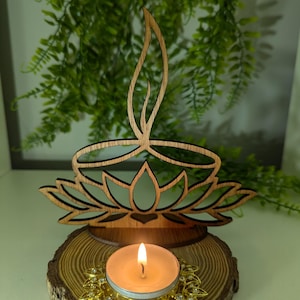 Könnte beinhalten: Ein Kerzenhalter aus Holz in Form einer Lotusblume mit einer brennenden Teelichtkerze in der Mitte. Der Kerzenhalter steht auf einer Holzscheibe mit einem goldenen Dekorrand.