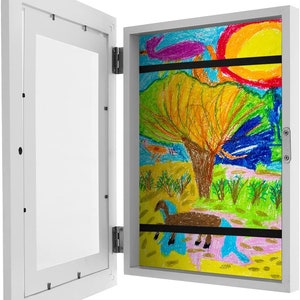 May include: White wooden picture frame with a hinged door that opens to reveal a colourful drawing of a landscape with a tree, sun, and animals. The drawing is done in crayon.