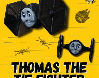 Può includere: Un giocattolo TIE fighter nero e grigio con la faccia di Thomas il Treno. Il giocattolo è su uno sfondo giallo con il testo "Thomas the TIE Fighter".