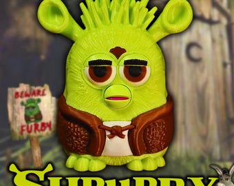 Puede incluir: Un juguete Furby verde con temática de Shrek con detalles marrones, que lleva un chaleco marrón y una camisa blanca. La palabra "SHRUBBY" está en la parte inferior, con un letrero que dice "BEWARE FURBY".