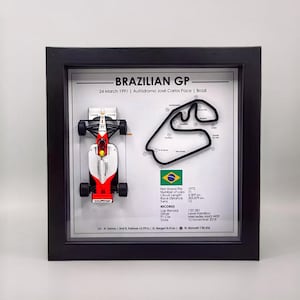 May include: A framed print of a red and white Formula 1 race car with a black track map and text that reads "BRAZILIAN GP 24 March 1991 | Autódromo José Carlos Pace | Brazil".