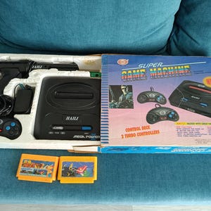以下が含まれることがあります： ヴィンテージのスーパーゲームマシンビデオゲームコンソールセット。セットには、黒いコンソール、2つのコントローラー、ライトガン、2つのゲームカートリッジが含まれています。ボックスには「Super Game Machine」と「Control Deck 2 Turbo Controllers」の文字があります。