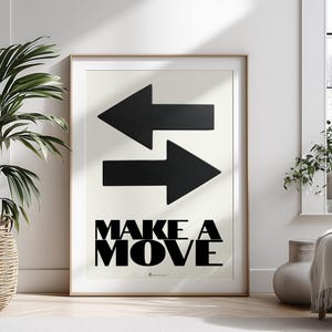 Könnte beinhalten: Gerahmter Kunstdruck mit zwei schwarzen Pfeilen, die in entgegengesetzte Richtungen zeigen. Darunter steht in schwarzer Schrift "MAKE A MOVE". Das Kunstwerk wird in einem hellen, modernen Innenraum präsentiert.