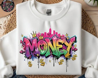 May include: White sweatshirt with a colorful graffiti design. The word "MONEY" is written in vibrant, multi-colored graffiti style, with dollar signs and a city skyline in the background. The design includes crowns, hearts, and stars.