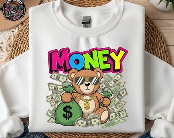May include: White sweatshirt with a colourful graphic that says "MONEY". The graphic features a brown teddy bear wearing sunglasses and a gold chain, holding a green money bag and surrounded by banknotes.