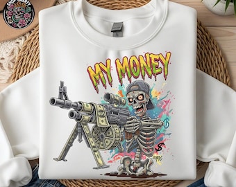 May include: White sweatshirt with a vibrant graphic of a skeleton wielding a machine gun constructed from banknotes. The phrase "MY MONEY" is displayed above the skeleton in a graffiti style. The design incorporates a baseball cap and colourful paint splatters.