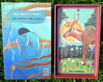 Może przedstawiać: Talia kart tarota w turkusowym i kasztanowym pudełku. Na okładce pudełka widnieje napis "The Gentle Tarot" i "Heal Yourself Heal The Earth". Talia zawiera kartę z ilustracją jelenia i napisem "The Empress". Talia jest autorstwa Mari in the Sky.