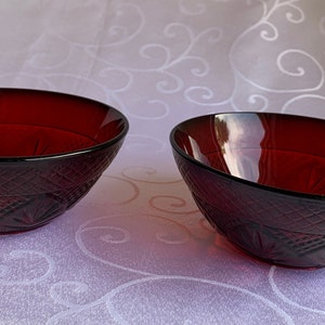 May include: Two red glass bowls with a diamond pattern on the outside. The bowls are empty and sitting on a white tablecloth.