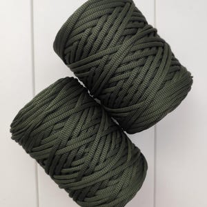 Op de afbeelding: Twee spoelen donkergroen koord tegen een witte achtergrond. Het koord is strak geweven, waardoor een textuur ontstaat. De spoelen zijn diagonaal geplaatst, wat de kleur en textuur van het materiaal benadrukt.