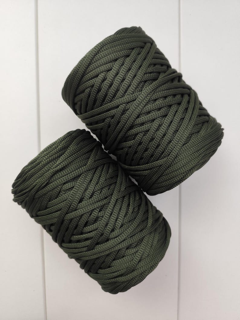 Op de afbeelding: Twee spoelen donkergroen koord tegen een witte achtergrond. Het koord is strak geweven, waardoor een textuur ontstaat. De spoelen zijn diagonaal geplaatst, wat de kleur en textuur van het materiaal benadrukt.