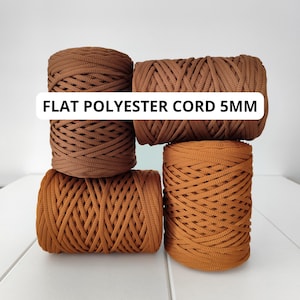 May include: Four spools of flat polyester cord in shades of brown and orange. The text "FLAT POLYESTER CORD 5MM" is displayed across the image. The cord is tightly wound, showcasing its texture and thickness, suitable for various crafting projects.