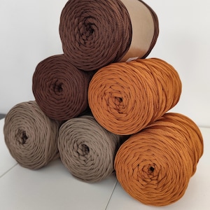 Op de afbeelding: Een stapel garen in verschillende bruin- en beigetinten. De kleuren vari&euml;ren van donkere chocolade tot lichtbeige, met enkele bollen in een warme, goudbruine tint. Het garen is strak opgerold, wat wijst op een gladde textuur, perfect voor knutselprojecten.