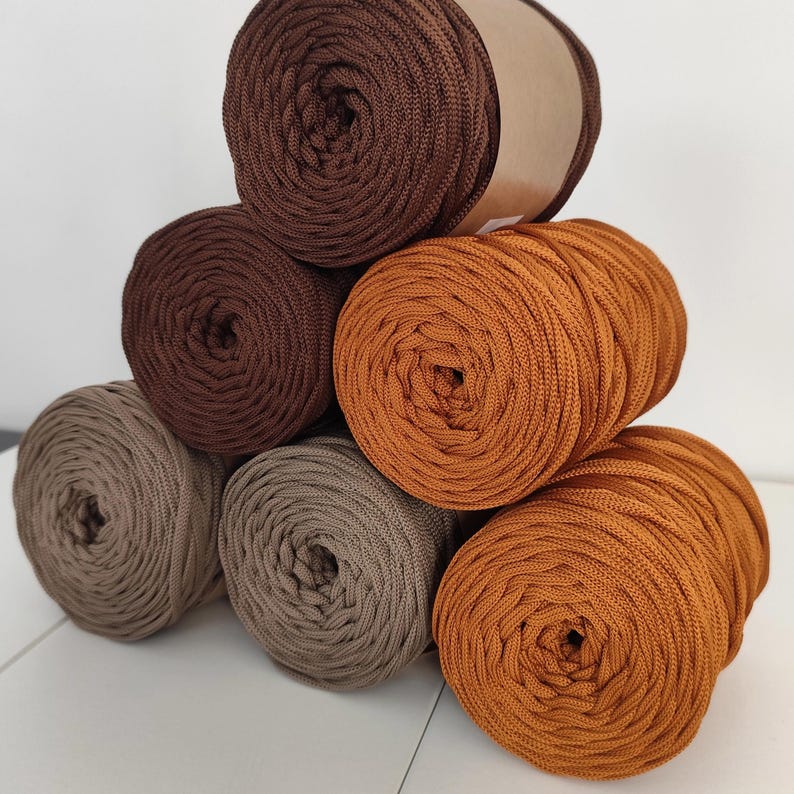 Op de afbeelding: Een stapel garen in verschillende bruin- en beigetinten. De kleuren vari&euml;ren van donkere chocolade tot lichtbeige, met enkele bollen in een warme, goudbruine tint. Het garen is strak opgerold, wat wijst op een gladde textuur, perfect voor knutselprojecten.