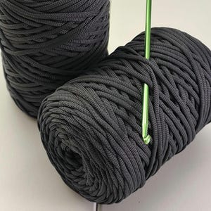 Può includere: Due bobine di paracord grigio scuro, una con un ago verde infilato.