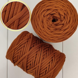 Op de afbeelding: Twee spoelen met bruin katoenen touwgaren. Het garen is dik en getextureerd, en de spoelen zijn strak gewikkeld.