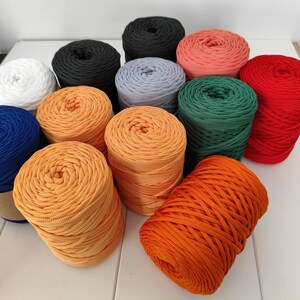 Op de afbeelding: Een verzameling kleurrijke garenbollen in verschillende tinten, waaronder wit, zwart, grijs, koraal, groen, rood, blauw en oranje. Het garen is netjes opgerold, wat suggereert dat het klaar is voor brei- of haakprojecten.
