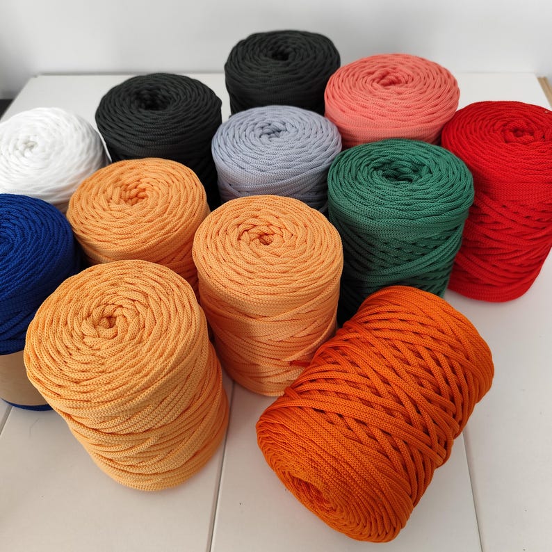 Op de afbeelding: Een verzameling kleurrijke garenbollen in verschillende tinten, waaronder wit, zwart, grijs, koraal, groen, rood, blauw en oranje. Het garen is netjes opgerold, wat suggereert dat het klaar is voor brei- of haakprojecten.