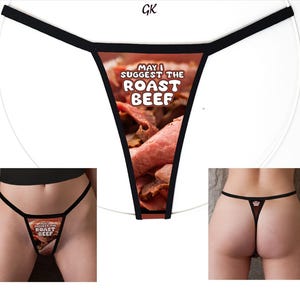 May include: A thong featuring a photographic print of sliced roast beef with the text "MAY I SUGGEST THE ROAST BEEF" in white letters. The garment has thin black elastic straps and a triangular front panel with a brown and pink meat pattern.