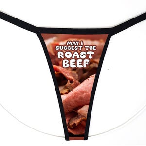 May include: A thong with a black waistband and trim featuring a central graphic print of sliced roast beef. The text printed in white letters over the meat image reads, "MAY I SUGGEST THE ROAST BEEF" in a bold, rounded, sans-serif font style.