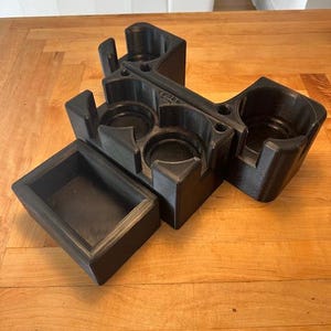 May include: Black 3D printed organizer with multiple compartments for holding small items. The organizer has a rectangular tray and a T-shaped section with four circular openings.