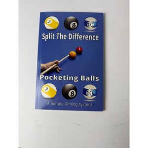 May include: A blue instructional book titled Split The Difference Pocketing Balls A Simple Aiming system. The cover features illustrations of billiard balls numbered 8, 9, and 10, along with a graphic of a pool cue tip touching a yellow ball.