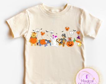 May include: A cream-coloured t-shirt with a Halloween graphic. The design features cartoon characters in costumes, including Winnie the Pooh as a pumpkin and Piglet as a ghost. The t-shirt has a round neck and short sleeves.