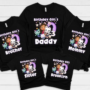 May include: Black t-shirts with a colourful graphic featuring a cartoon girl, a white cat, and the number 3. Text on the shirts reads "Birthday Girl's" and names like "Daddy", "Mommy", "Brother", "Sister", and "Brooklyn".