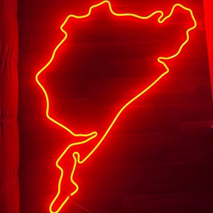 Könnte beinhalten: Ein neongelber Umriss einer Rennstrecke vor rotem Hintergrund. Das Neonlicht hat die Form einer Karte einer Rennstrecke. Das Bild wird vom Neonlicht beleuchtet.