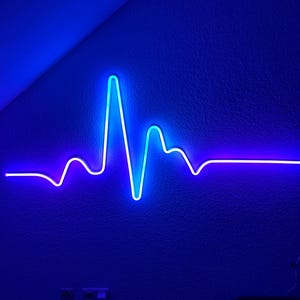 Può includere: Una luce al neon blu e viola a forma di battito cardiaco. La luce è montata su un muro.