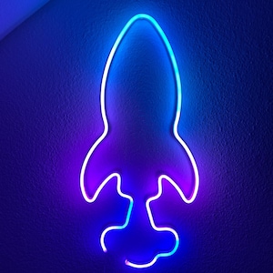 Puede incluir: Una lámpara de neón azul y púrpura en forma de cohete en una pared azul oscuro.